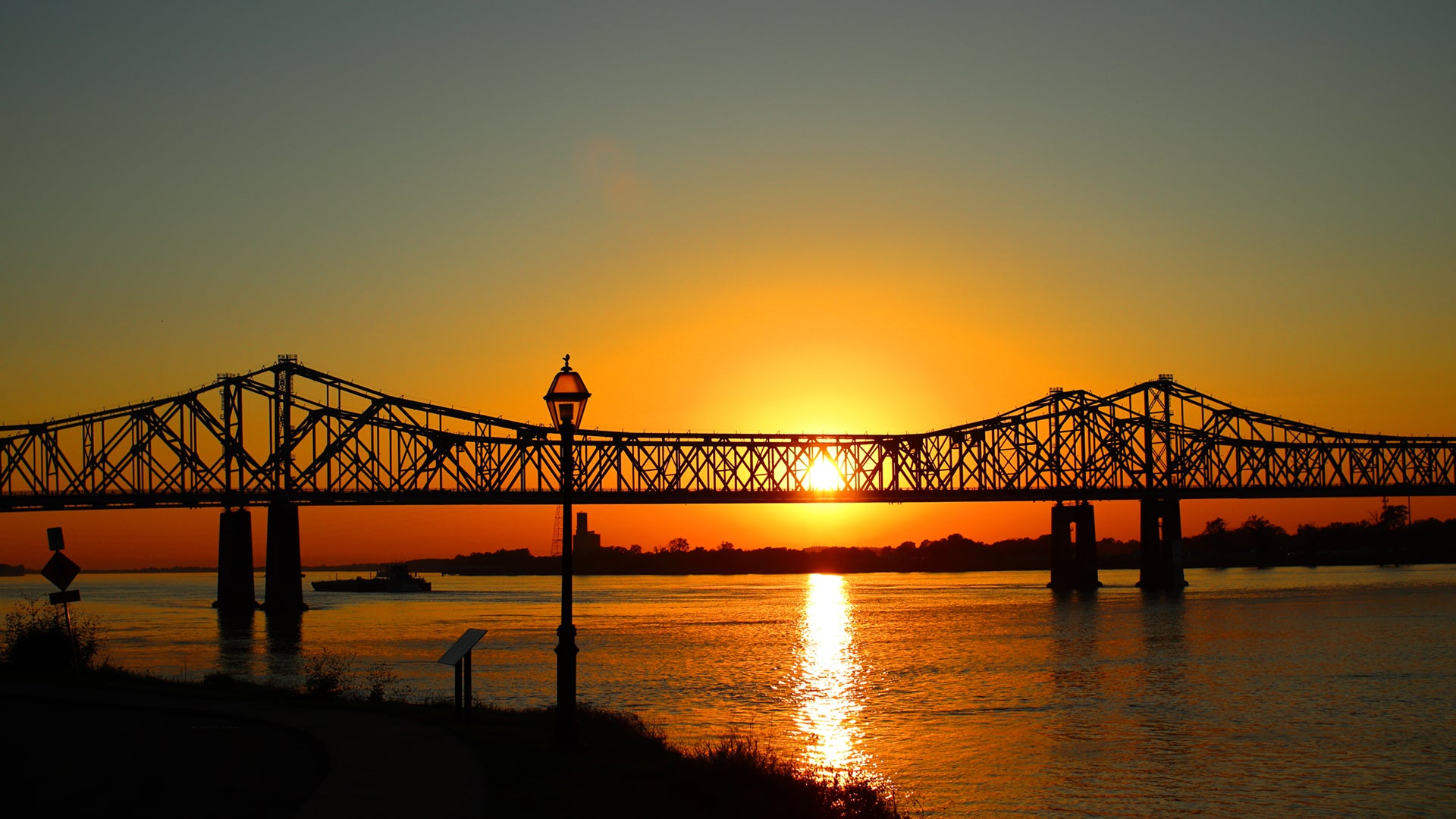 Sunset over a bridge with a silhouette of a street lamp in the foreground.