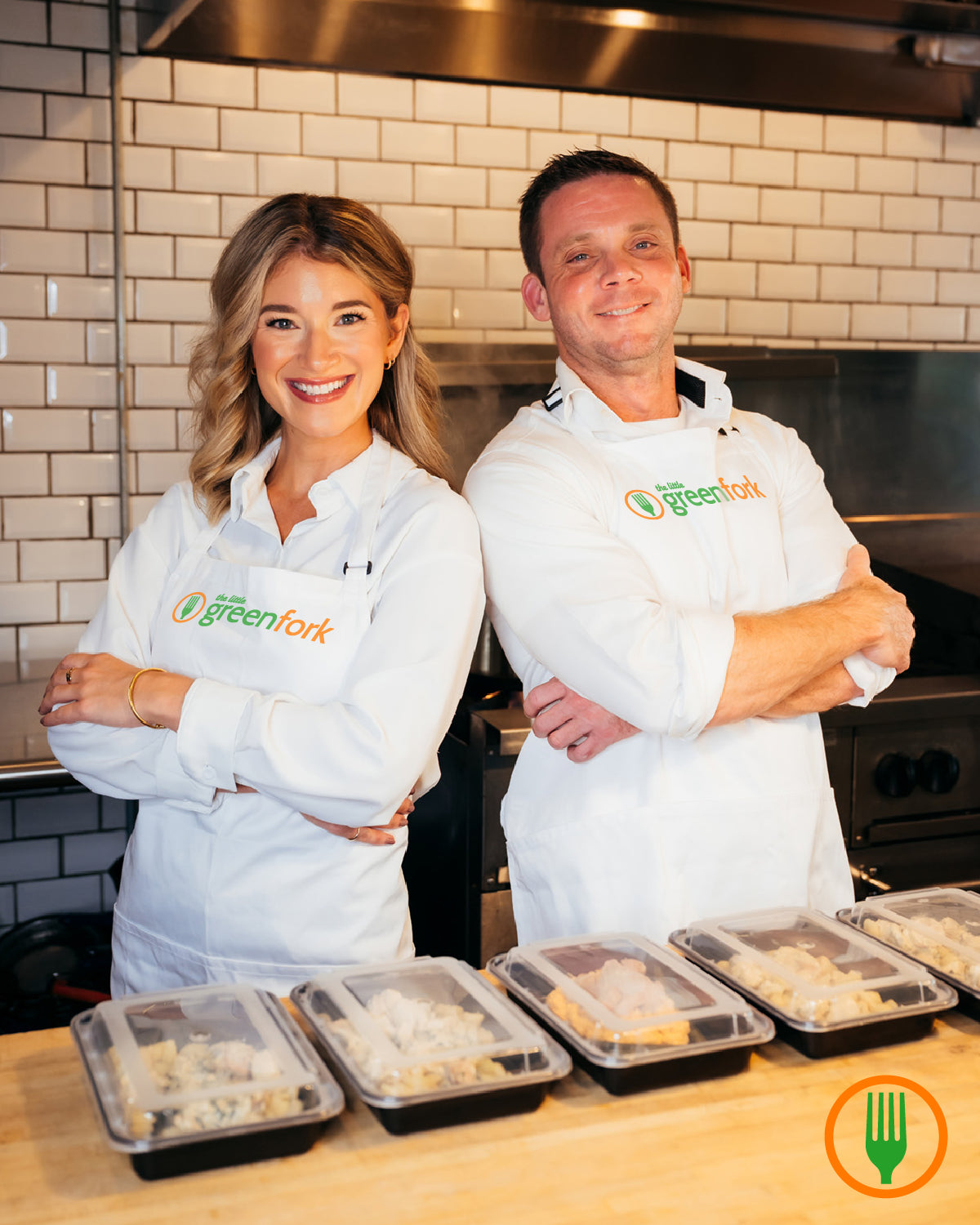 Two people wearing 'Greenfork' aprons standing behind containers of food in a kitchen.
