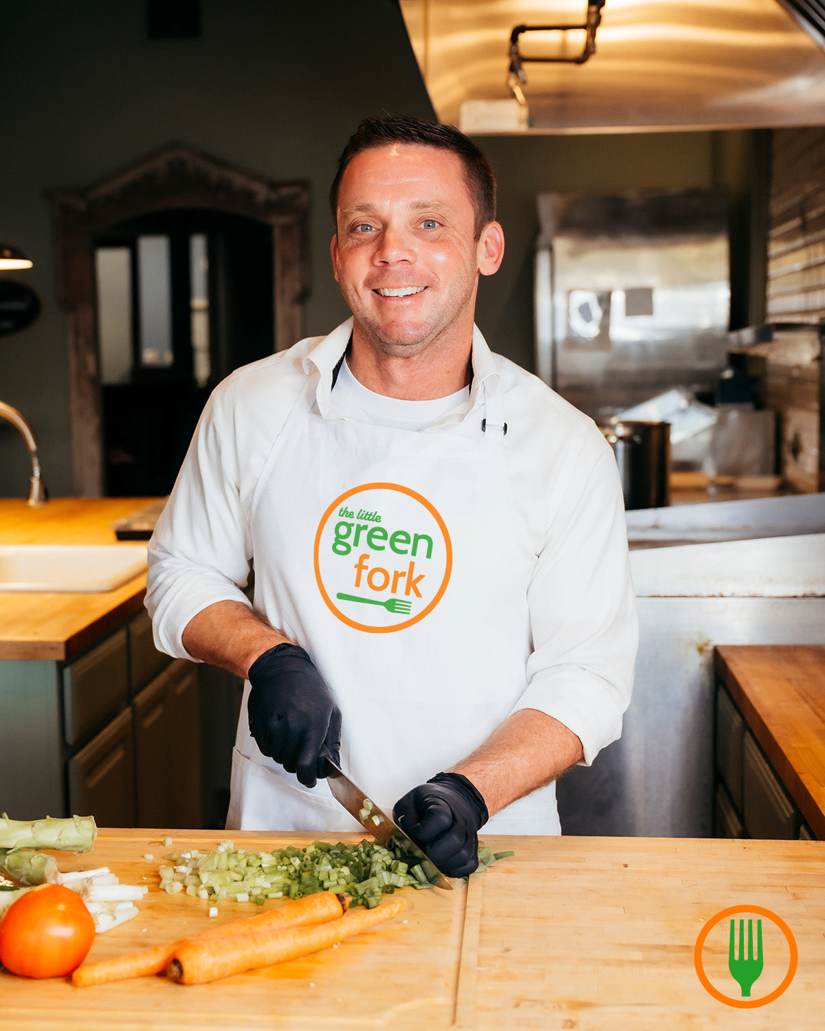 Man in a kitchen wearing a 'Green Fork' apron, preparing food.
